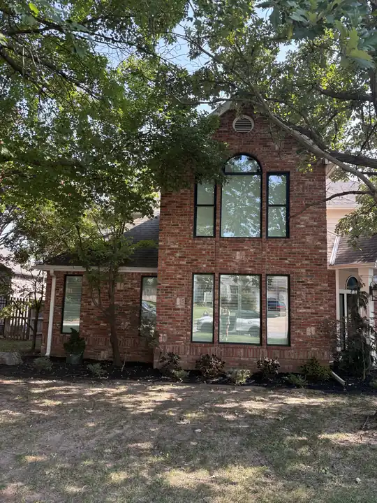 Red brick home with new black-frame windows behind a large shade tree