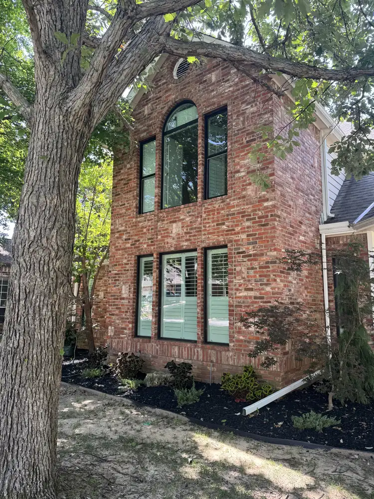 Two-story red brick home with new black-frame windows and an arched top window