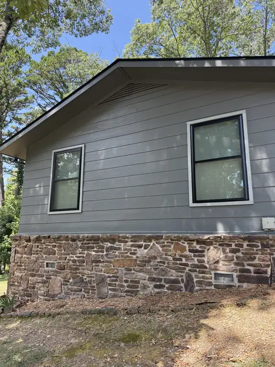 Gray siding gable wall with two new black-frame double-hung windows above a stone base