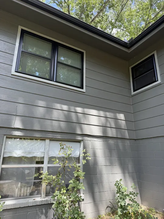 After: the same gray-sided home with new black-frame windows and white trim