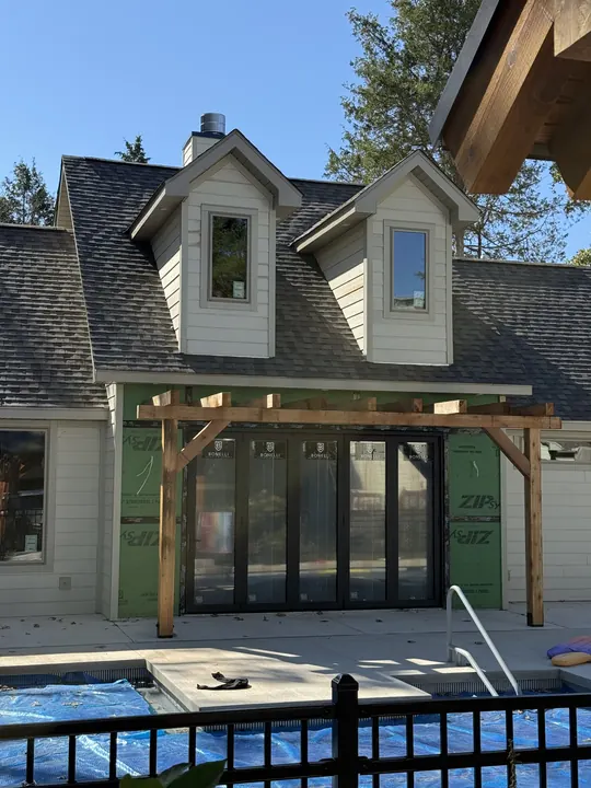 Black multi-panel glass doors under a cedar pergola beside a pool