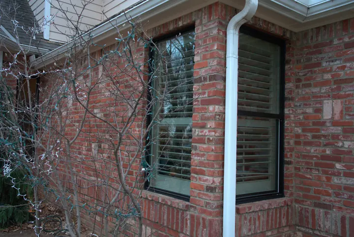 Two new black-frame windows on the corner of a red brick home