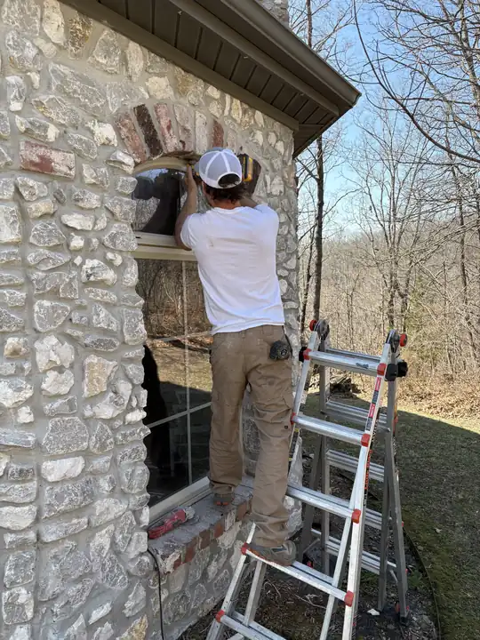 Installer on a ladder fitting a window into a stone home