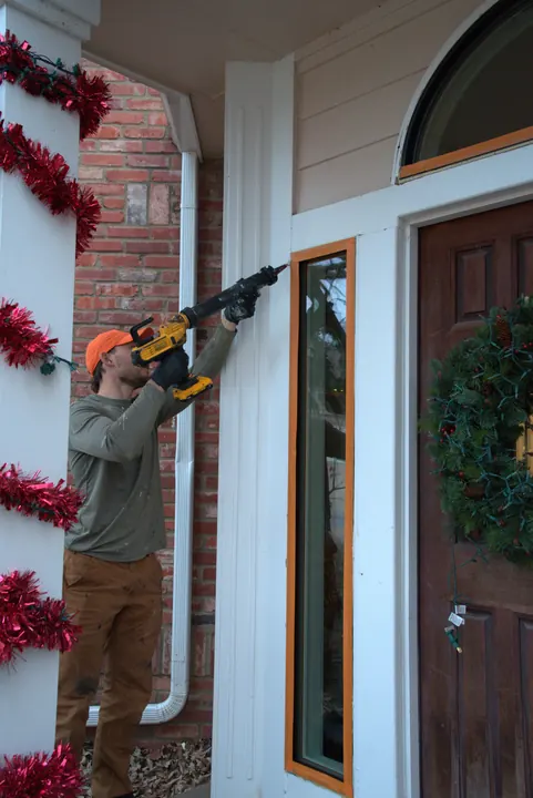 Installer sealing around a new narrow black-frame window beside a front door