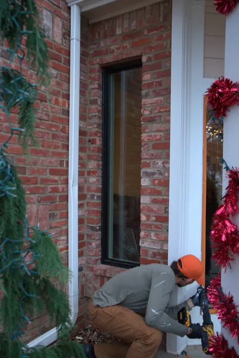 Installer finishing the trim below a new narrow black-frame window on a brick home