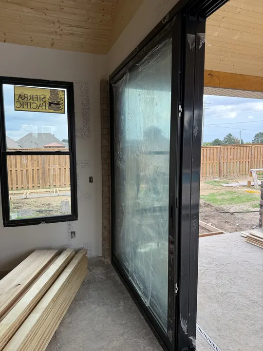Large black-frame glass door panel being installed in a home under construction