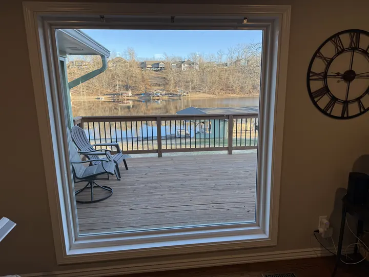 Interior view through a large picture window to a deck and lake