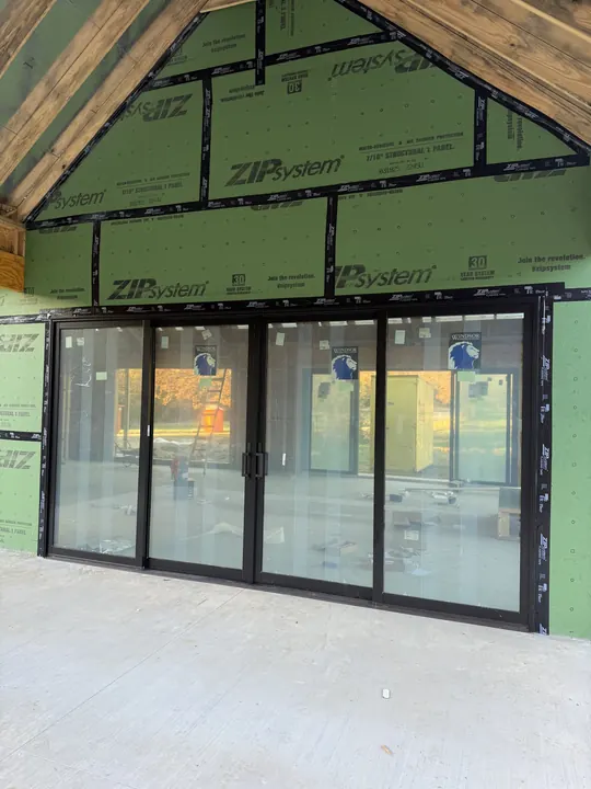 Four-panel black sliding glass doors installed in a house-wrapped wall