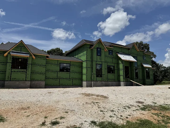 Home under construction wrapped in green sheathing with its windows installed