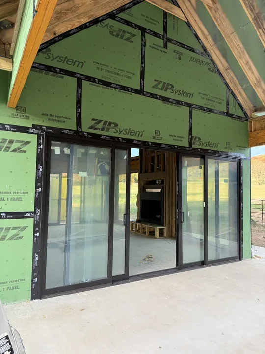 Black sliding glass doors under a gable on a home wrapped in green sheathing
