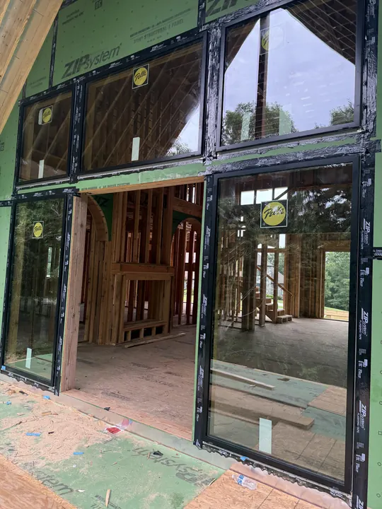 Black-frame window wall and doors in a gable on a home under construction