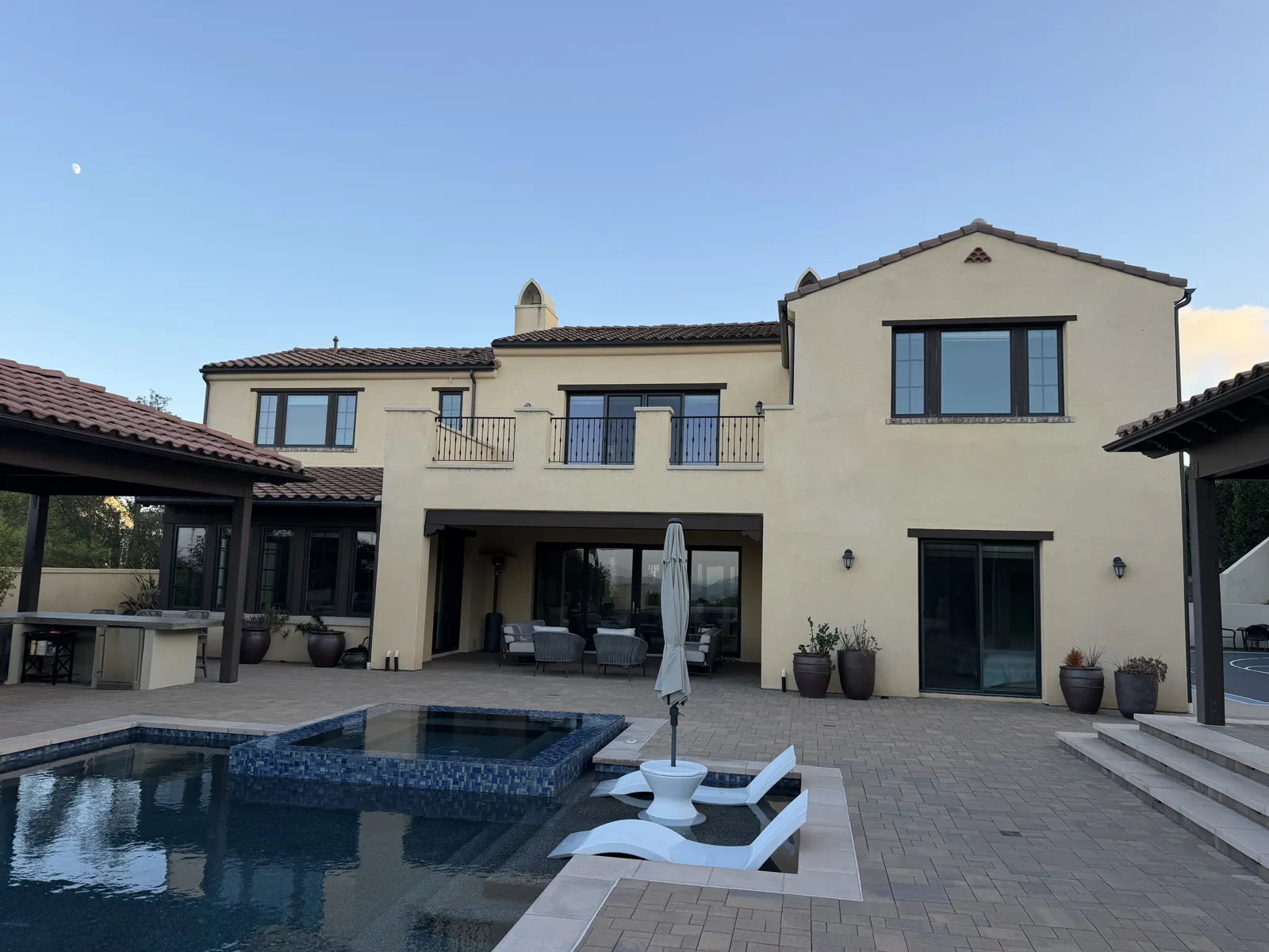 Large two-story stucco home with dark-frame windows and patio doors overlooking a backyard pool